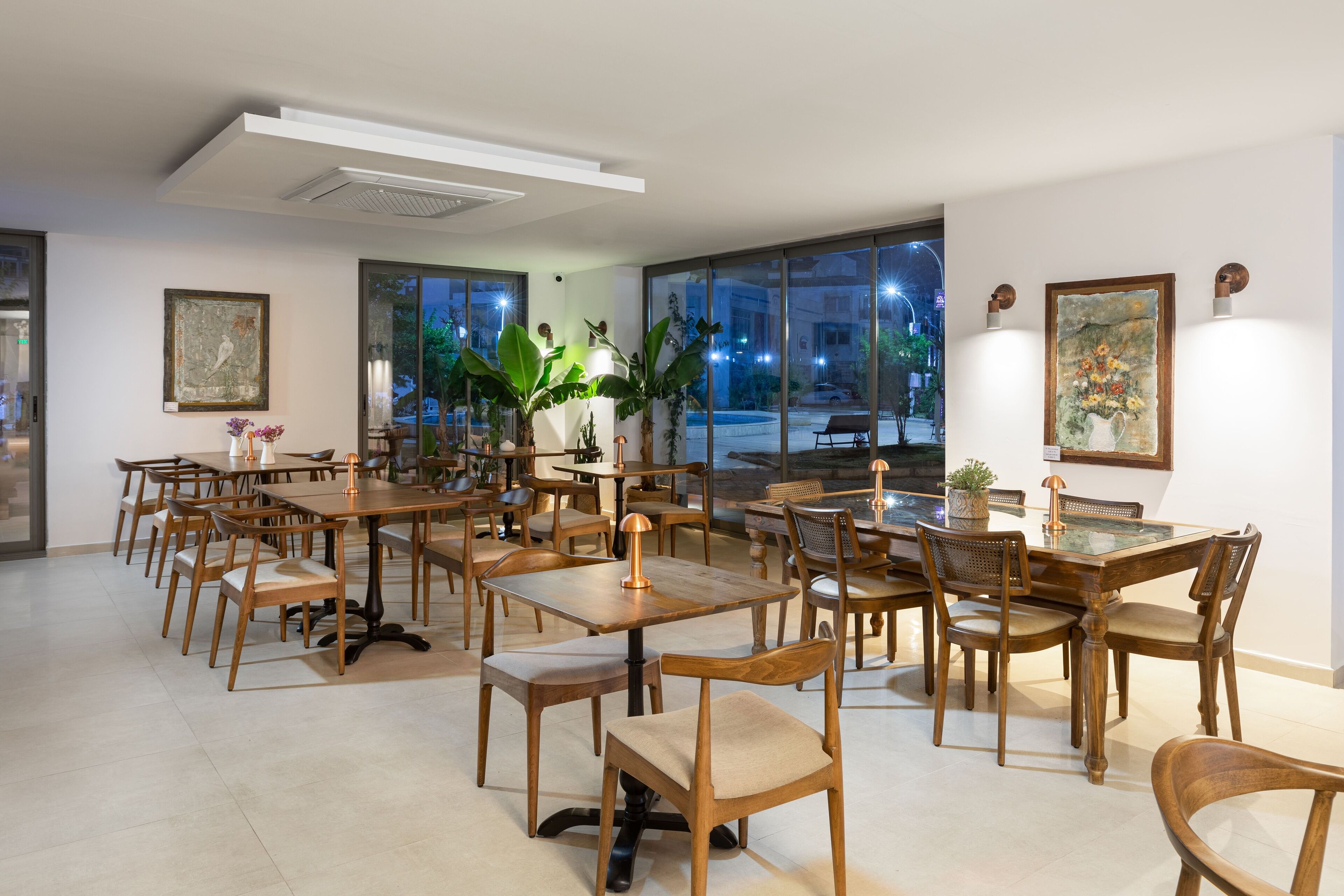 Un'ampia sala da pranzo con diversi tavoli e sedie in legno, grandi finestre con vista sulla città e lampade moderne.