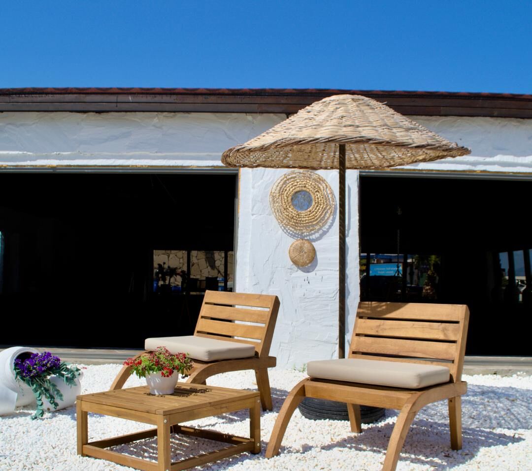 Two wooden lounge chairs with cushions, a woven parasol, and a small table with a potted plant.