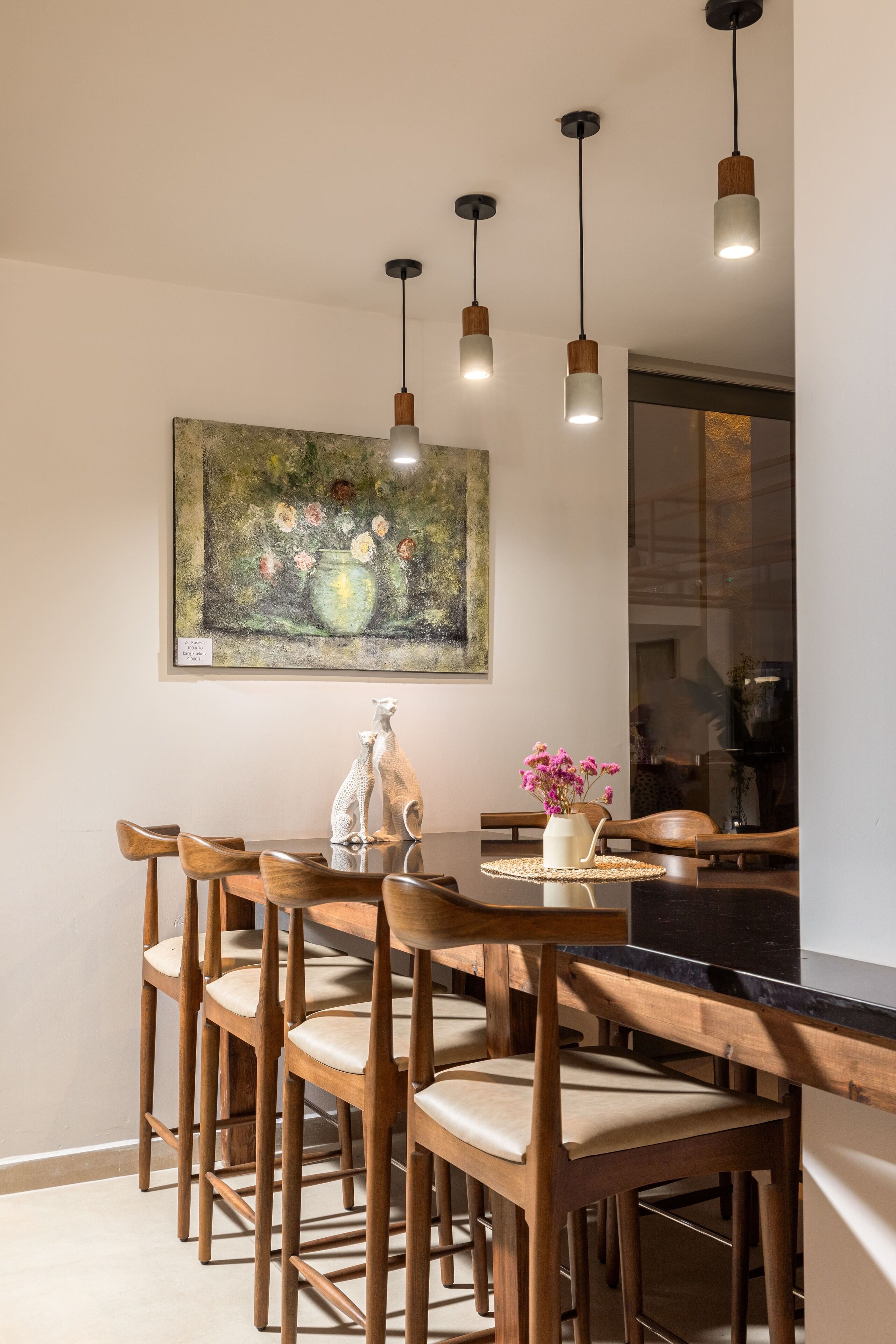 Un comedor con sillas de madera y una mesa, un cuadro en la pared y lámparas colgantes.