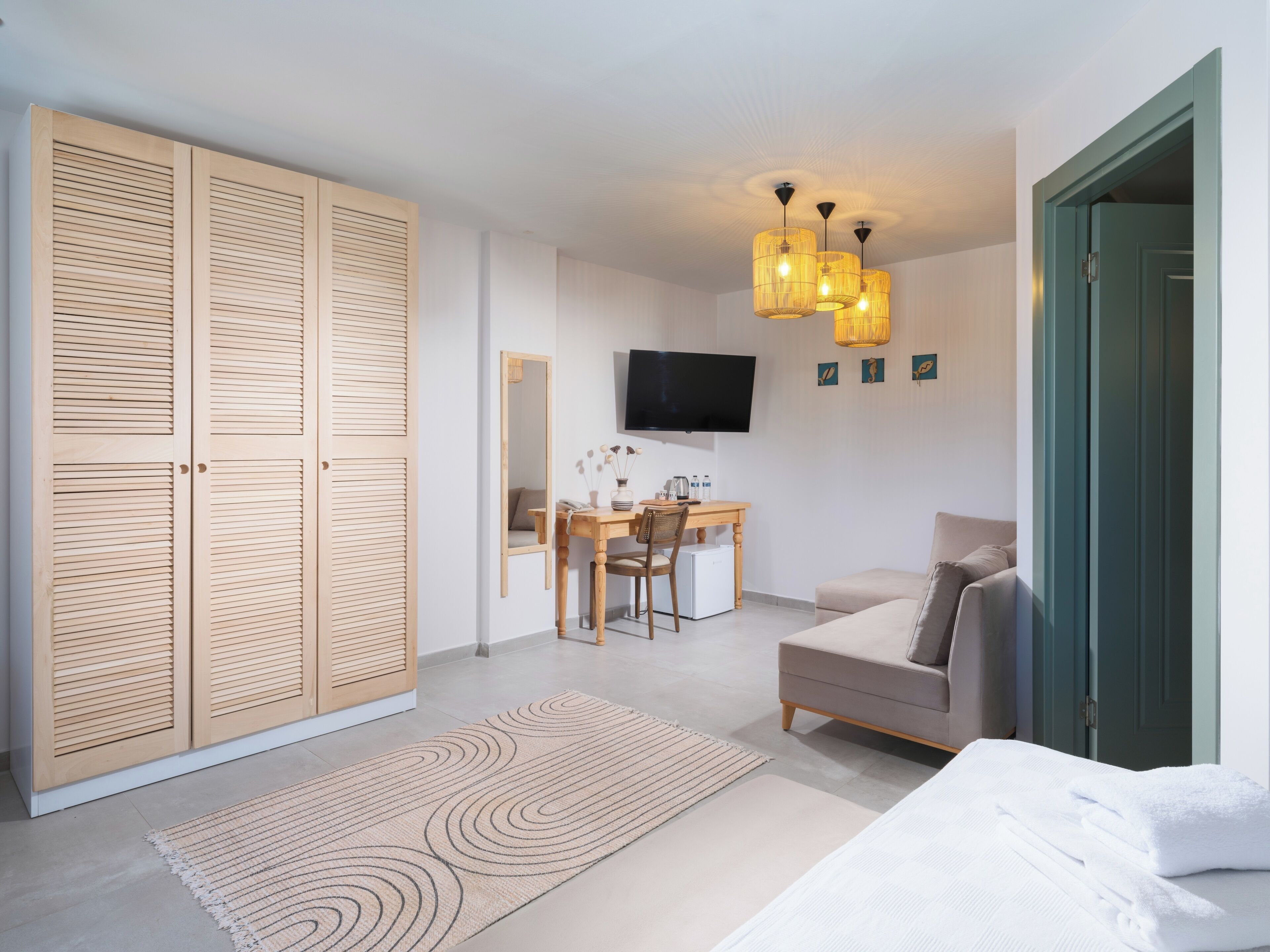 A modern bedroom with a large wardrobe, a desk with a chair, a television, and a sofa.
