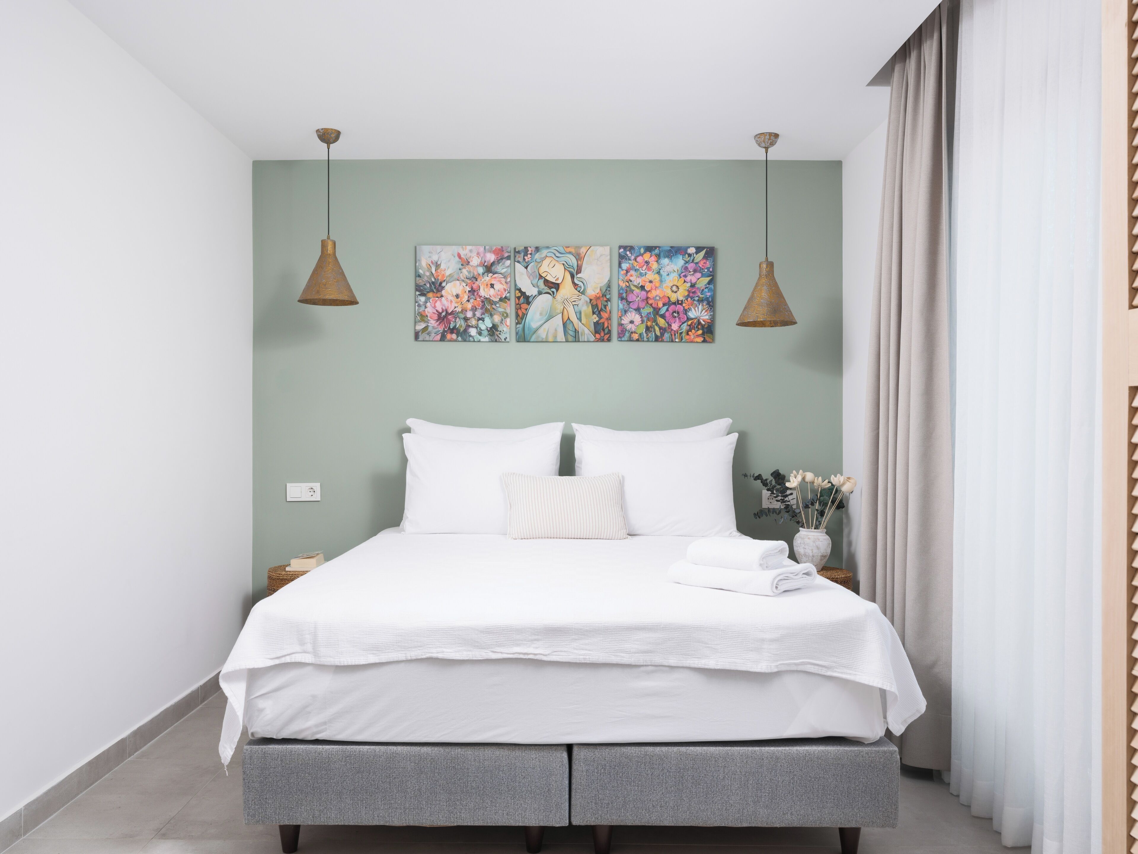 Un dormitorio moderno con una cama, dos lámparas de pared y tres cuadros florales.
