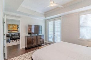 Relax in this serene bedroom with a large bed, ceiling fan, flat-screen TV, and a large window with blinds.