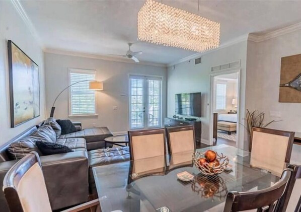 Relax in this stylish living room with a glass dining table, comfortable seating, and a mounted TV.