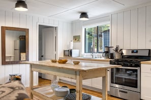 A modern kitchen with white cabinetry, a wooden table, a stove, and a microwave.