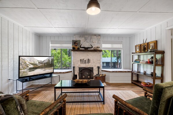 A cozy living room with a stone fireplace, wooden furniture, and a television on a stand.