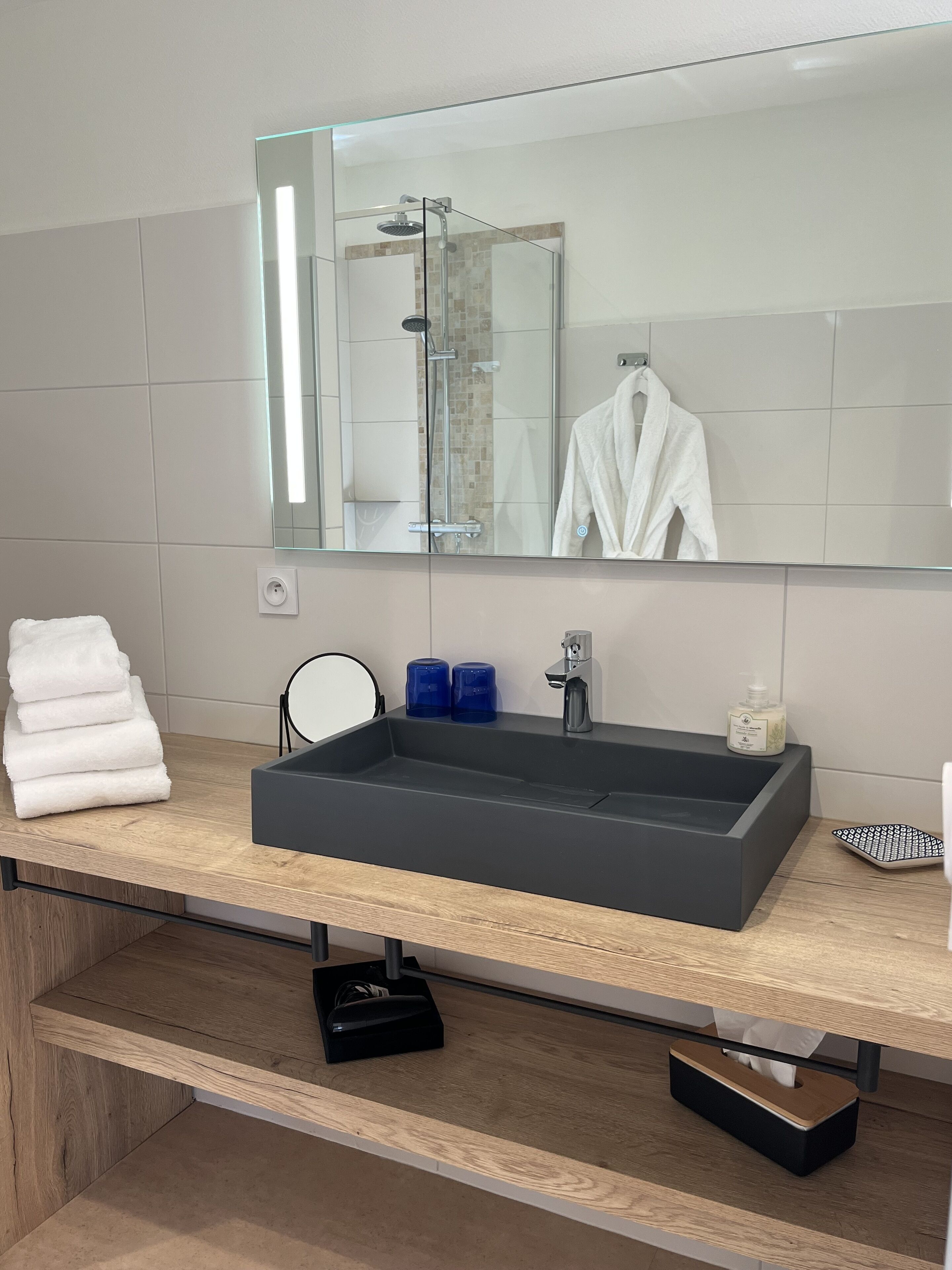 A modern bathroom with a large mirror, a rectangular sink, and a glass-enclosed shower.