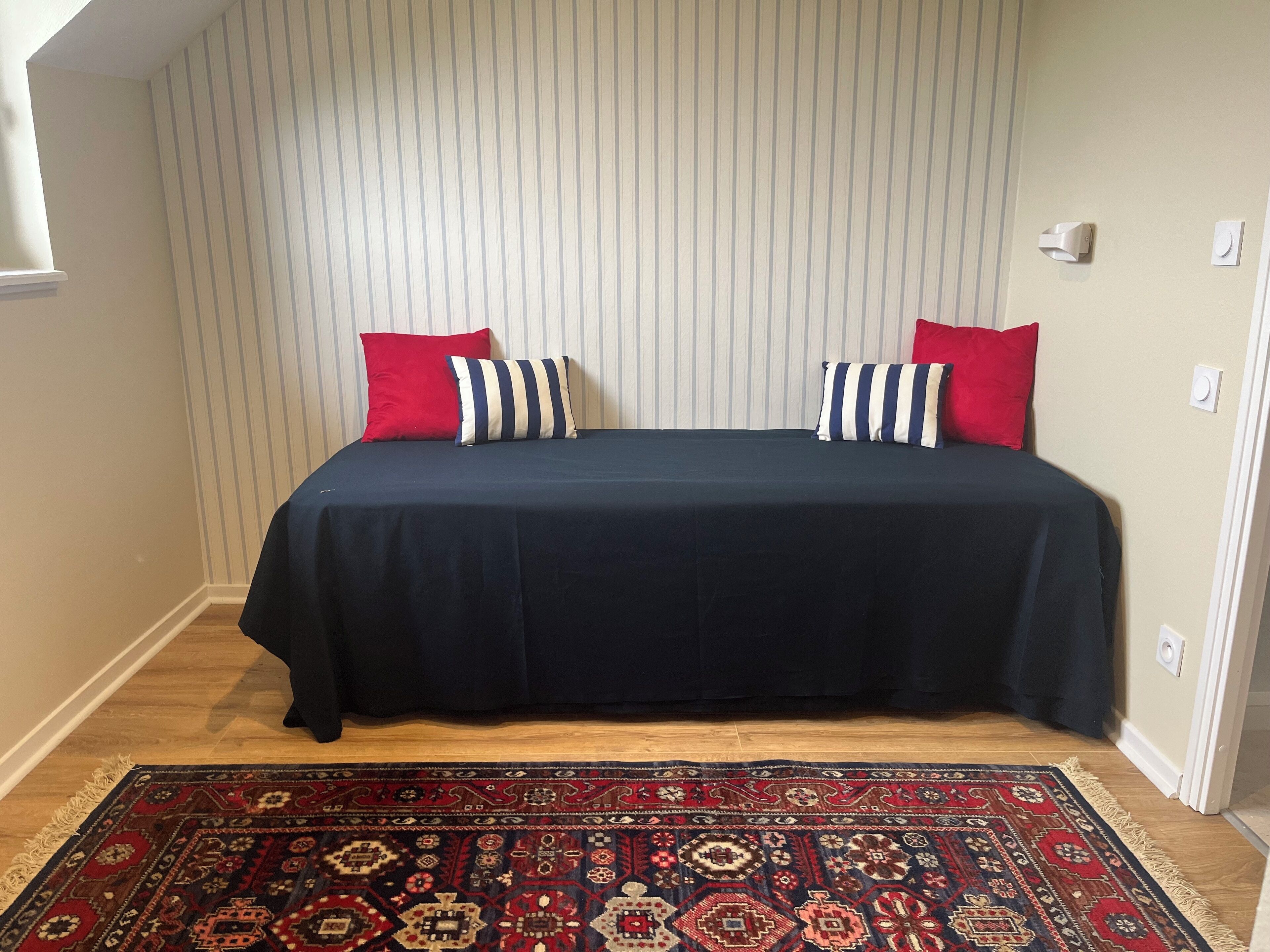 Une chambre à coucher avec un lit, des coussins à rayures, un tapis à motifs et un mur à rayures.