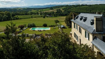 A large house with a swimming pool, surrounded by lush green fields and mountains in the background.