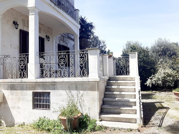 A white building with a balcony, a staircase, and a garden area. - Ancient tower in the countryside, surrounded by greenery, 6 km from Ostuni (Br). (Ostuni)