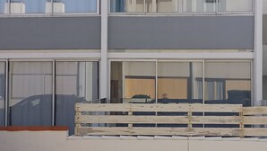 A multi-story building with large windows, a balcony, and a flat roof.