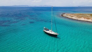 Eine Segelyacht ankert in klarem türkisblauem Wasser, im Hintergrund eine Küstenlinie und Berge.