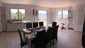 A spacious dining area with a large table and chairs, a kitchen area with a sink and cabinets, and large windows offering a view of the outdoors.