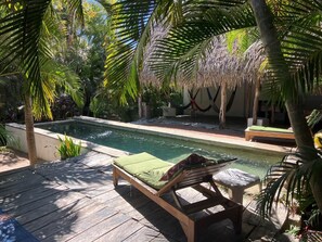 Relax by the serene pool surrounded by lush tropical foliage and shaded by palm trees.