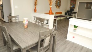 A dining area with a wooden table and chairs, a white counter with decorative vases, and a small shelf with a plant.