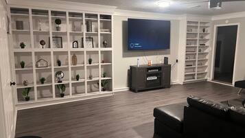 A living room with a flat-screen TV mounted on the wall, a dark wooden entertainment unit, and a black leather sofa.