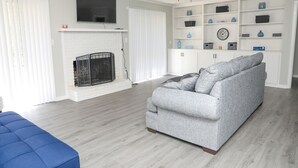 A living room with a grey sofa, a blue ottoman, a fireplace, and a TV mounted above it.