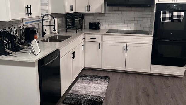 A modern kitchen with white cabinetry, a black stove, and a black dishwasher.
