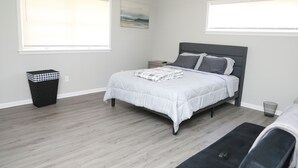 A bedroom with a bed, a nightstand, a trash can, and a window.