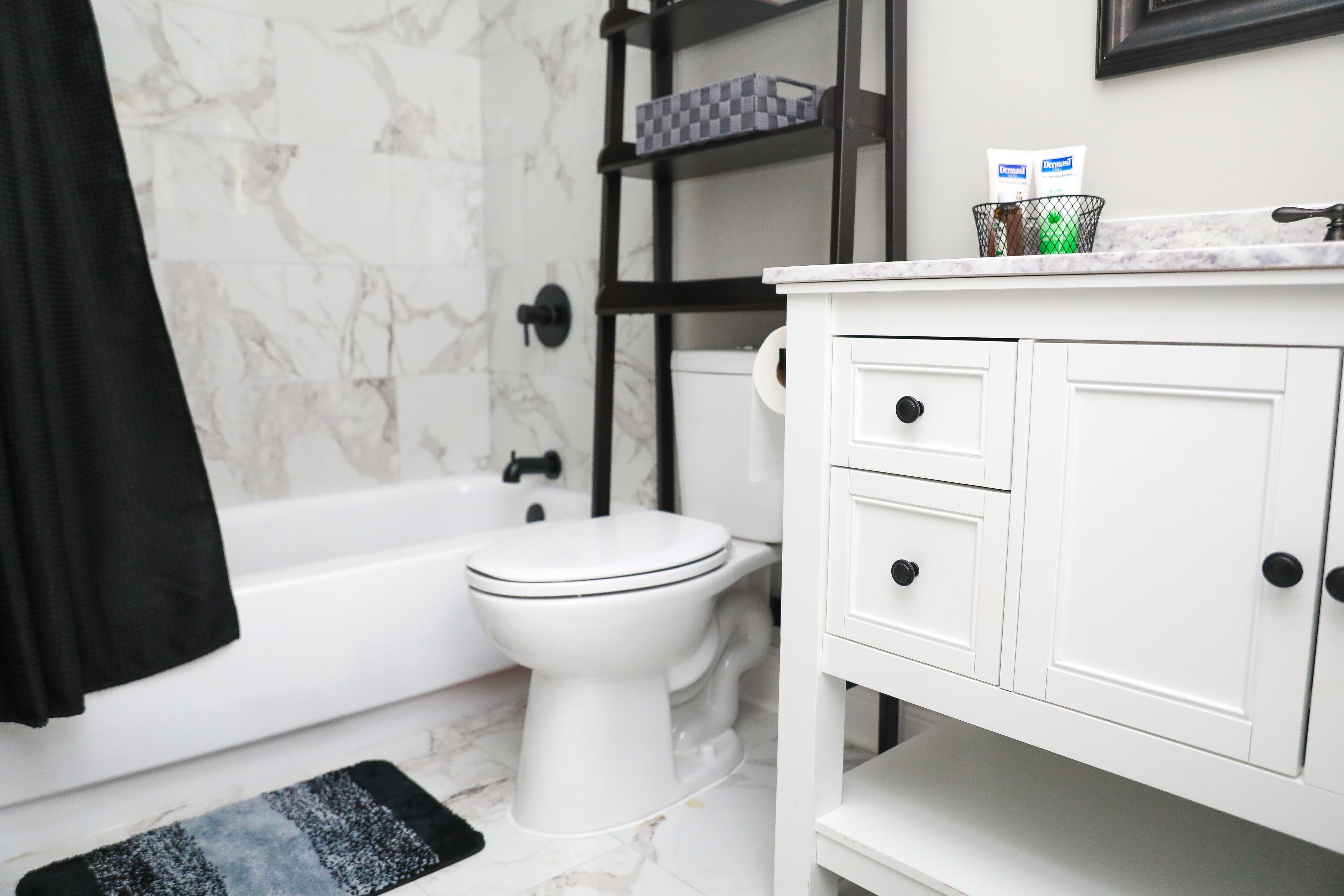 A bathroom with a white toilet, a black towel, a marble shower wall, and a white vanity with drawers.