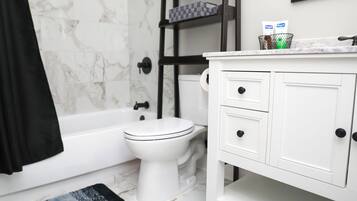 A bathroom with a white toilet, a black towel, a marble shower wall, and a white vanity with drawers.