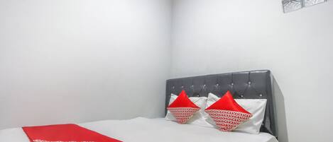 A neatly made bed with a red and white patterned bedspread, a grey upholstered headboard, and two red pillows with white text.