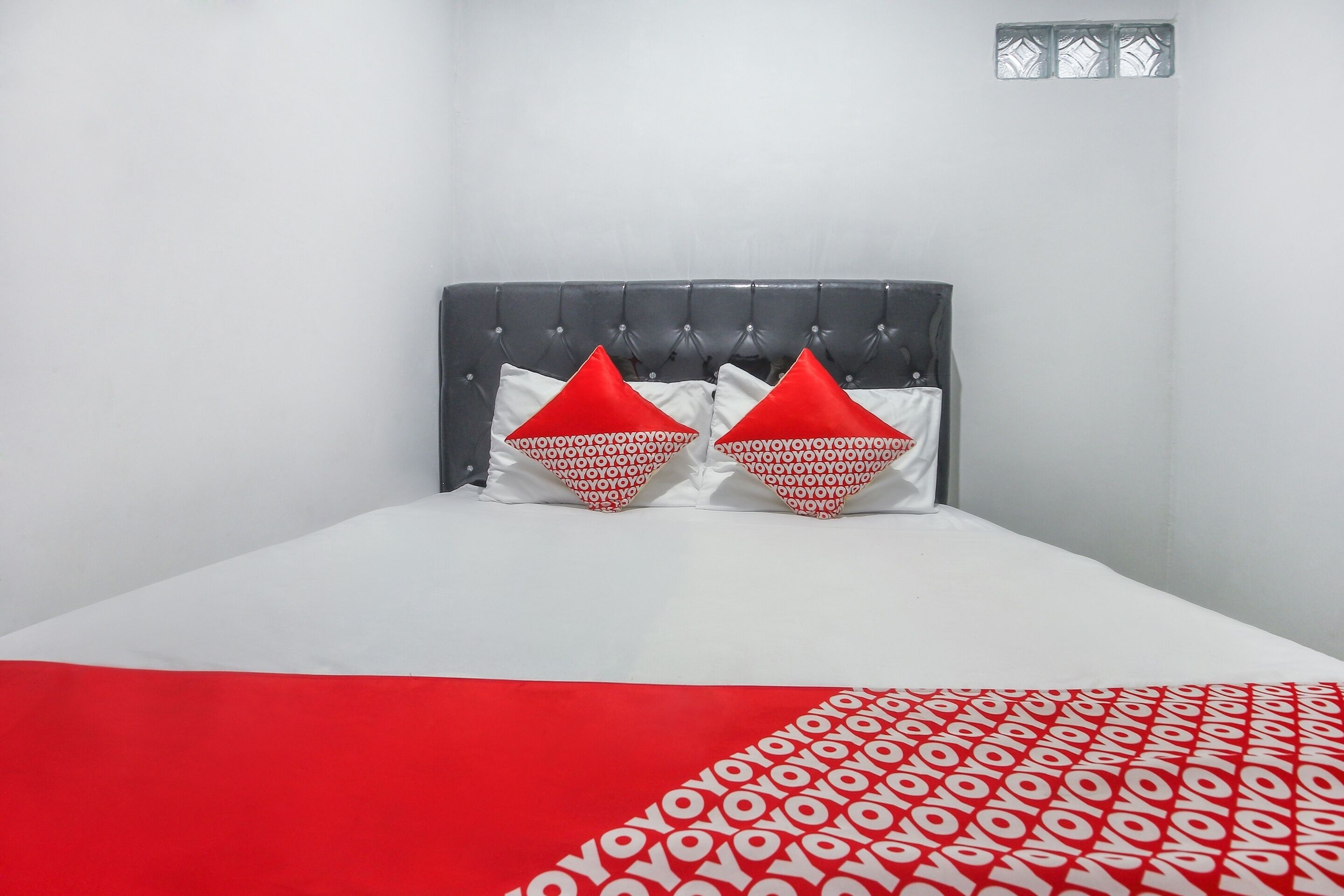 Ein Bett mit einer Bettdecke in Weiß und Rot mit Muster, zwei rote Kissen ebenfalls mit Muster und ein grauer, gepolsterter Kopfteil.