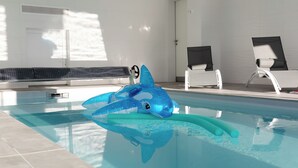 Une piscine avec un flotteur en forme de requin bleu, des murs carrelés et deux chaises longues blanches.