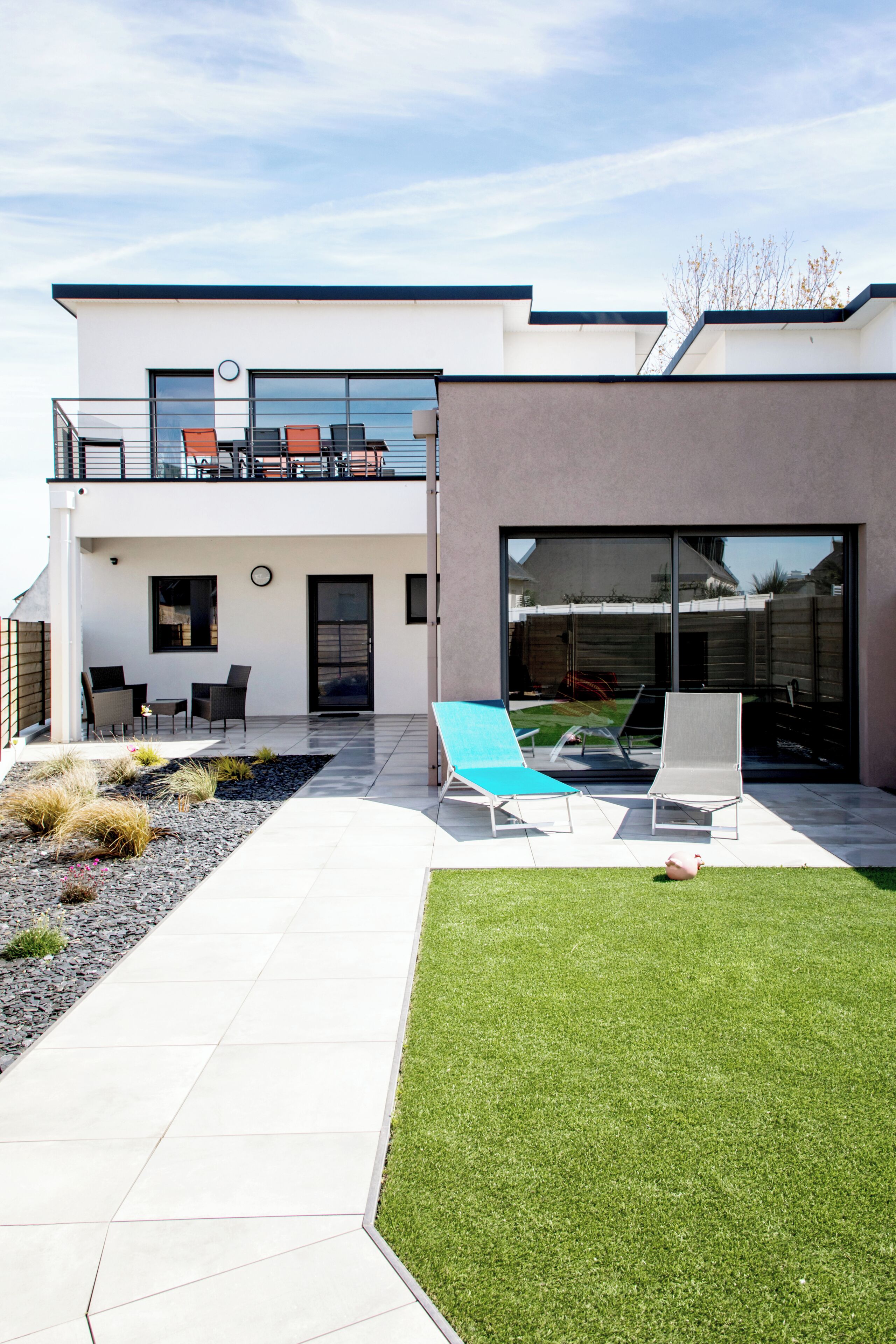 A modern two-story house with a patio, outdoor seating, and a well-maintained lawn.