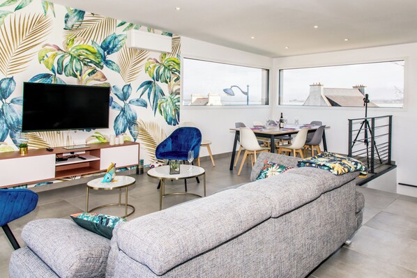 A modern living room with a flat-screen TV, a sofa, a dining table, and chairs. - Villa Elisa Bretagne Pool SPA (Sibiril)