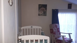 A room with a crib, a chair, a window with curtains, and a framed picture on the wall. - Appartement 4pers (Naussac Fontanes)