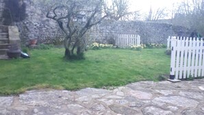 A stone-paved patio with a white picket fence and a small tree in the center. - Appartement 4pers (Naussac Fontanes)