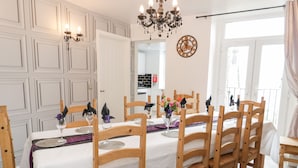 Un coin repas avec une table blanche dressée pour six personnes, des chaises en bois et un lustre.