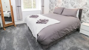 Une chambre à coucher avec un lit, un miroir, une fen être et un mur orné d’un motif floral.