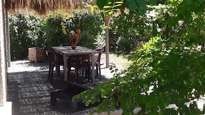An outdoor patio with a table and chairs, surrounded by greenery and a thatched roof structure. - Maison 5/6 Pers Piscine Prive sur 6000 m2 (quissac)