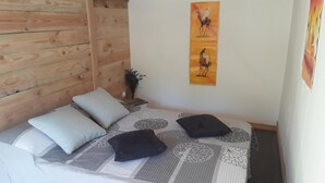 A bedroom with a wooden headboard, a bed with patterned bedding, two pillows, a nightstand with a plant, and a wall with a painting. - Maison 5/6 Pers Piscine Prive sur 6000 m2 (quissac)