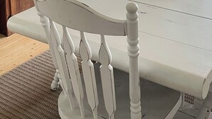 Un coin repas avec une table et des chaises blanches, une tête de cerf accrochée au mur et des étagères remplies d’ustensiles de cuisine.