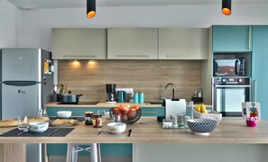 A modern kitchen with a wooden countertop, stainless steel appliances, and teal cabinetry.