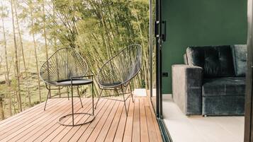 Um deck de madeira com duas cadeiras de arame e um sofá cinzento em frente a uma parede verde.