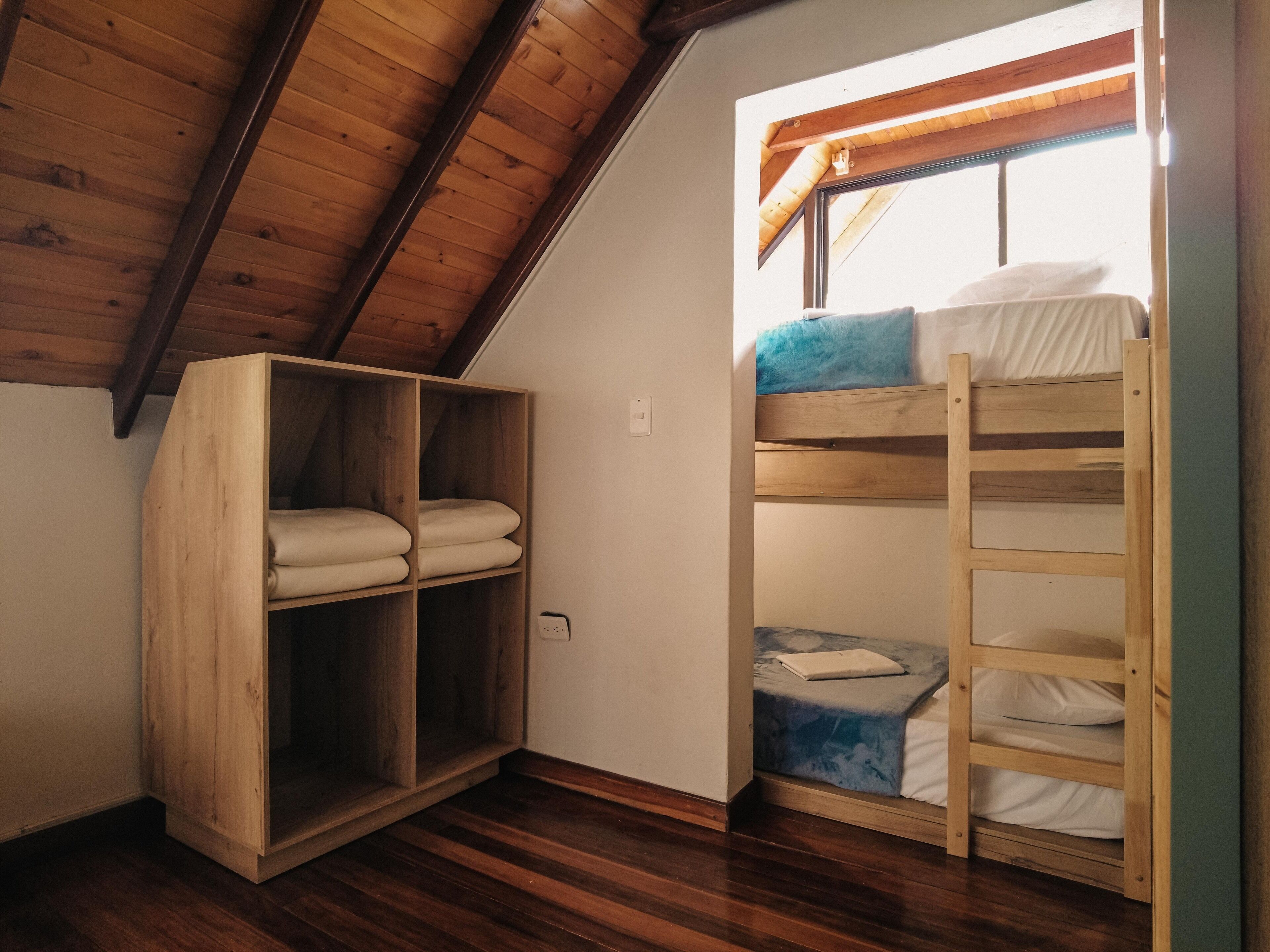 Ein Schlafsaalzimmer mit einem Holzbett, einem Schrank aus Holz und einer schrägen Decke.