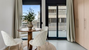 A modern room with a round table, two white chairs, a vase with a plant, and a view through large windows. - Sanders Port - Majest Studio With Roof-top Terrace (Piraeus)