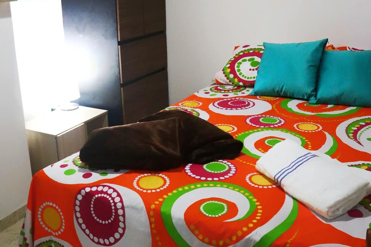A bed with a colorful patterned bedspread, a brown pillow, and a blue pillow.