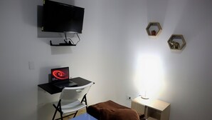Una habitación pequeña con escritorio, una silla, un televisor fijado en la pared y dos adornos hexagonales en la pared.