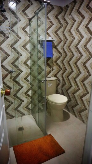 A bathroom with a herringbone patterned wall, a glass shower enclosure, a toilet, and a blue towel hanging on a rack. - HOSTAL KASAMADOR (Cali)