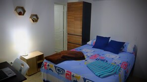 A bedroom with a bed, a desk with a laptop, a wardrobe, and two wall-mounted shelves with decorative items. - HOSTAL KASAMADOR (Cali)