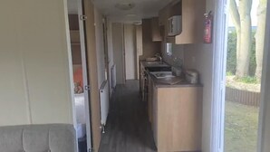 A narrow corridor leading to a compact kitchenette with a sink, a microwave, and a small countertop. A fire extinguisher is mounted on the wall. - 3 Bedroom Caravan Near Mablethorpe (Louth)
