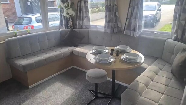 A corner seating area with a round table set for four, a small stool, and a vase with flowers. - 3 Bedroom Caravan Near Mablethorpe (Louth)