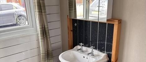 A bathroom with a white pedestal sink, a mirror above it, and a window with a curtain.