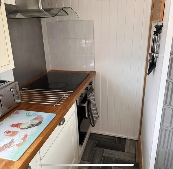 A compact kitchen with a built-in stove, a drying rack, and a small countertop with a decorative mat.