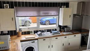 A compact kitchen with a washing machine, a sink, and a window with a view of a car. - D5 Rickardos Holiday Lets (Mablethorpe)