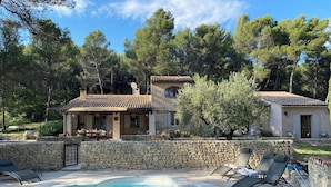 A stone-walled swimming pool with lounge chairs, a stone house with a tiled roof, and surrounding trees. - Large Mas in the Roussillon pine forest, heated swimming pool (Gargas)